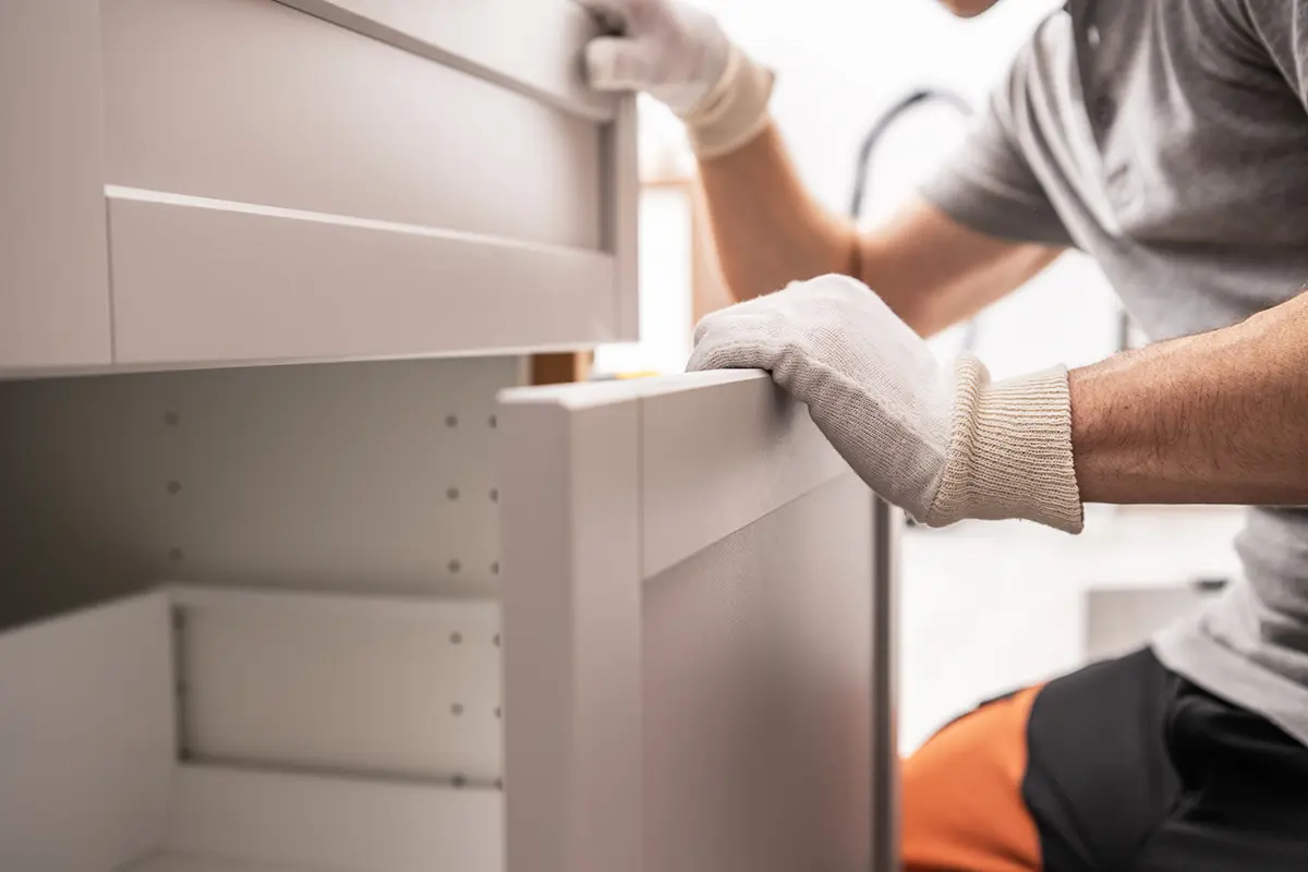 Küchenfronten erneuern Ein Mann in Handschuhen öffnet einen Schrank.