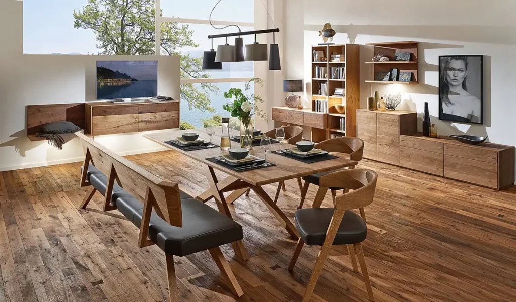 Wohnen - Esstisch aus Holz mit Kreuzbeinen gepolsterten braunen Lederstühlen und Bank mit niedrigen Regalen dahinter