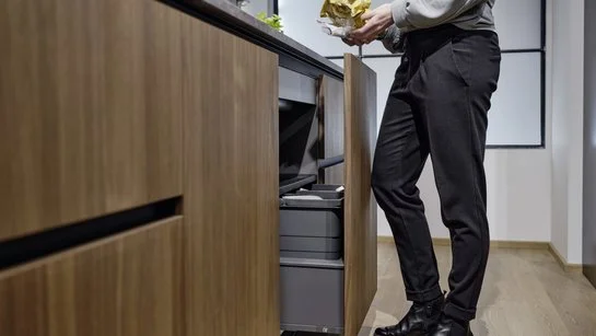 ewe Touch & Drive System Frau in der Küche mit Abfall in der Hand vor Unterschrank mit automatischem Müllsystem