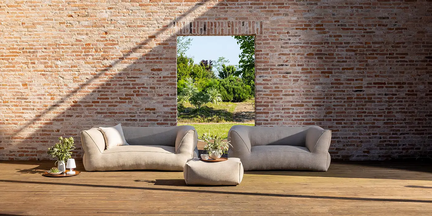 wv - Outdoor-Paradies Zwei weiche Sofas und ein Pouf stehen auf einer Terrasse vor einer Ziegelwand