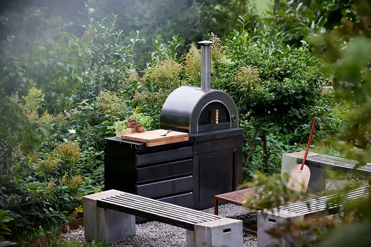 wv - Outdoorküche - myoutdoorkitchen-black-collection-phoenix Eine schwarz-weiße Außenküche mit einer Bank, umgeben von Pflanzen und einem einladenden Ambiente